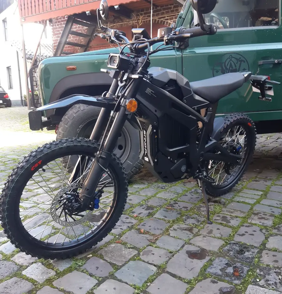 Schwarze Talaria Sting E-Enduro vor grünem Land Rover Defender